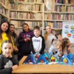 na zdjęciu widać dzieci w sali bibliotecznej stojących na tle regału z książkami