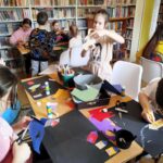 Przy stołach w sali bibliotecznej siedzą dzieci i wykonuja prace plastyczne