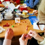 na zdjęciu widać panie seniorki siedzące wokół stołu w sali bibliotecznej i wykonujące korale