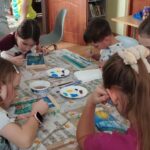 Przy stołach w sali bibliotecznej dzieci siedza przy stołach i wykonują prace plastyczne.