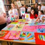 Dzieci przedszkolne w sali bibliotecznej prezentują wykonane przez siebie prace - wyklejankina kolorowych papierach.