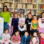 Na tle regałów stoją dzieci wraz z paniami bibliotekarkami i wychowawczynią