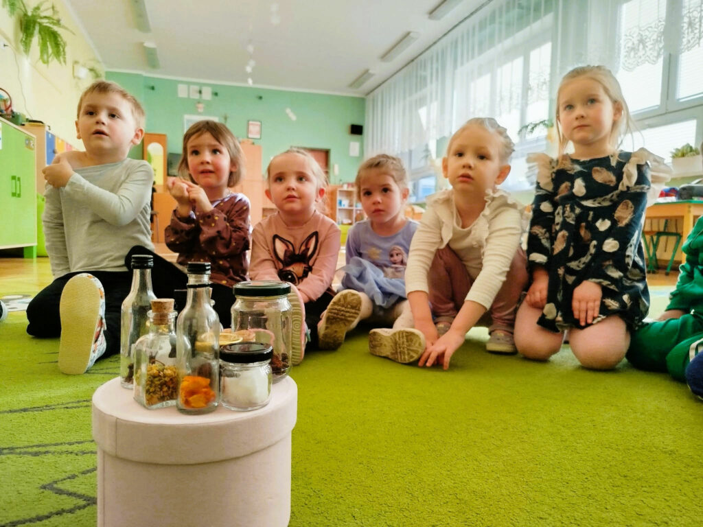 na zdjęciu widać dzieci siedzące na podłodze a przed nimi małe buteleczki