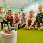 na zdjęciu widać dzieci siedzące na podłodze a przed nimi małe buteleczki