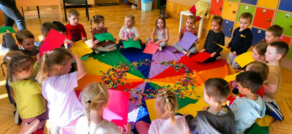 na zdjęciu widać dzieci siedzące wokół kolorowej chusty
