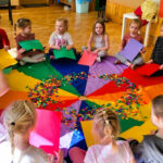 na zdjęciu widać dzieci siedzące wokół kolorowej chusty