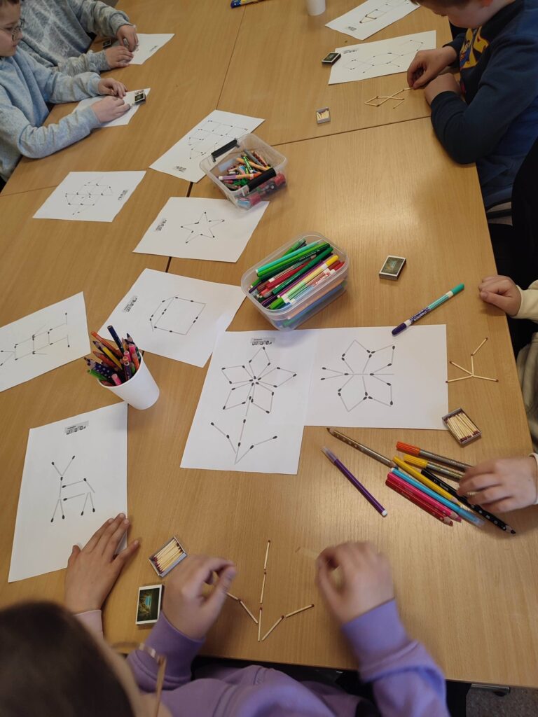 Na stole porozkładane karty z zabawali logicznymi. widać flamastry, kredki oraz dzieciece ręce , które wykonuja zagadki.