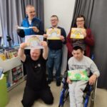 pięc osób na tle zasłony szarej prezentuje wykonane przez siebie prace. Jeden chłopiec siedzi na wózku inwalidzkim