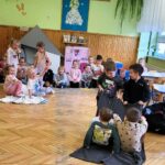 Na ziemi siedza dzieci w sali przedszkolnej. Czterech chłopców uczestniczy w dyscyplinie dwóch chłopców siedzi na kocyku i dwóch ich ciągnie .