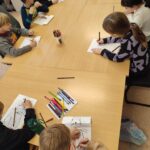 Ptzy stole wsali bibliotecznej siedza dzieci uczestniczce w lekcji bibliotecznej i wykonujące prace plastyczne Kapibarę