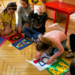 na zdjęciu widać dzieci siedzące na podłodze i oglądające kolorowe literki