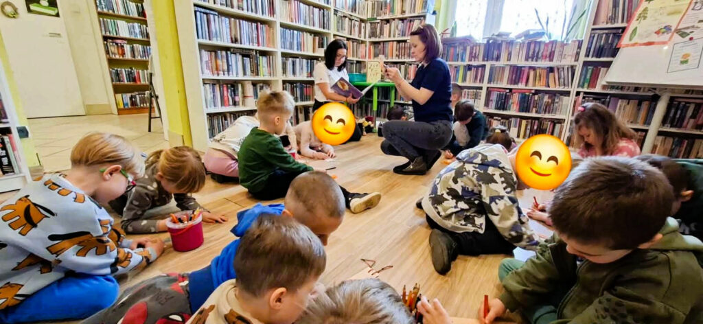 na zdjęciu widać dzieci siedzące na podłodze w sali bibliotecznej