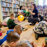 na zdjęciu widać dzieci siedzące na podłodze w sali bibliotecznej