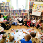 na zdjęciu widać dzieci siedzące na podłodze w sali bibliotecznej wokół książek