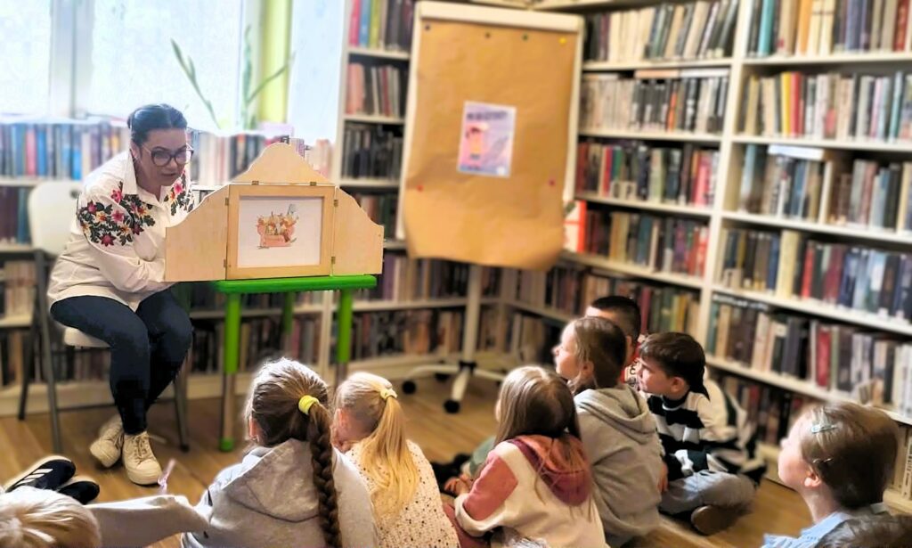na zdjęciu widać kobietę czytającą dzieciom książkę w formie teatrzyku Kamishibai