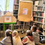 na zdjęciu widać kobietę czytającą dzieciom książkę w formie teatrzyku Kamishibai