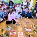 na zdjęciu widać dzieci siedzące na podłodze a przed nimi poukładane książki