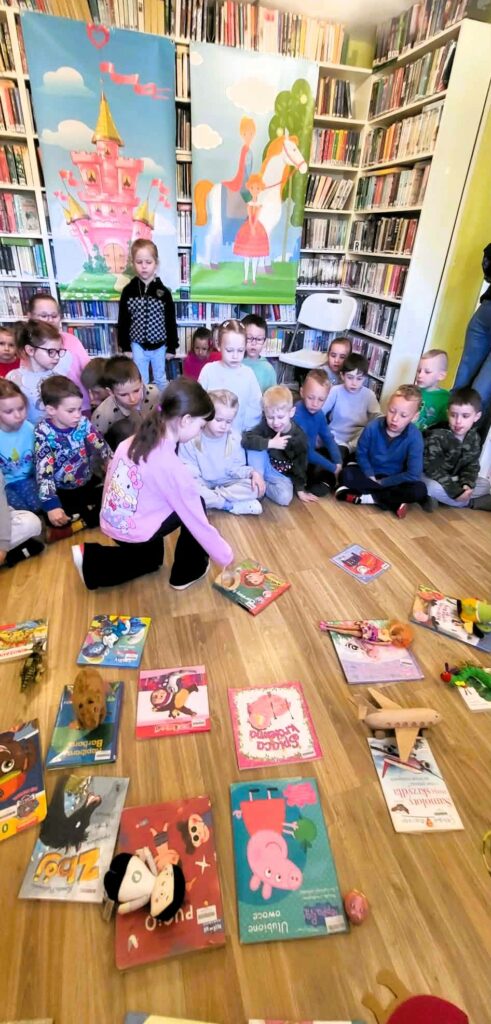 na zdjęciu widać dzieci siedzące na podłodze a przed nimi poukładane książki