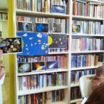 na zdjęciu widać bibliotekarkę pokazująca dzieciom zdjęcia przedstawiające kosmos
