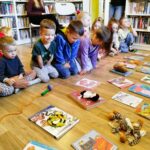 na zdjęciu widać dzieci na podłodze w sali bibliotecznej a przed nimi poukładane zabawki