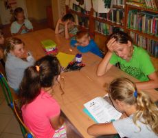 dzieci w czasie wakacyjnych zajęć w bibliotece słuchają opowiadania czytanego przez jedną z uczestniczek