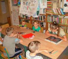 dzieci uczestniczące w wakacyjnych zajęciach z uwagą słuchają opowieści o  skarpetce czytanej przez jedną z dziewczynek