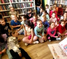 na zdjęciu widać dzieci w sali bibliotecznej siedzące na podłodze