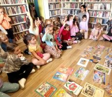 na zdjęciu widać dzieci w sali bibliotecznej, siedzące na podłodze a przed nimi kolorowe ilustracje